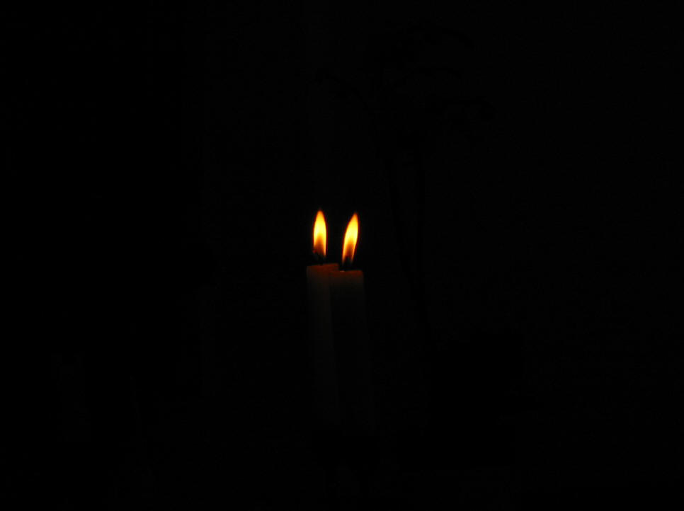 Two candle flames glow in the darkness.