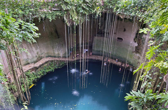 A large round opening in the ground with a pool of blue water below